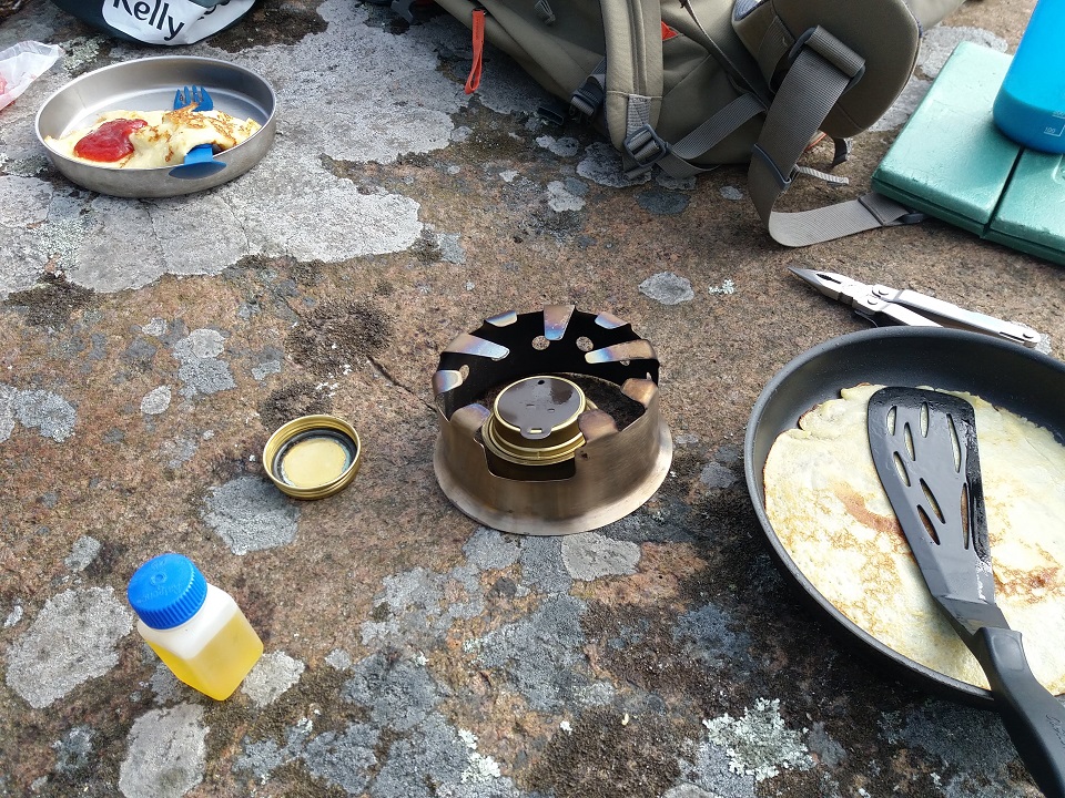 Fishing trip (Sweden). Using hobostove with alcohol burner to make pancakes, and boiling water with Kelly Kettle for coffee and warm dishing water. Pine cones a few feet away as fuel